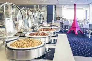 Buffet-Tisch mit verschiedenen Speisen, darunter gebratener Speck, Waffeln und eine pinke Eiffelturm-Skulptur im Hintergrund.