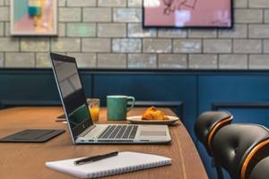 Laptop auf Konferenztisch im ReMIX Hotel mit Kaffee, Croissant und Notizbuch