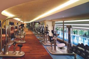 Innenansicht des Fitnesscenters im Titanic Mardan Palace mit Cardiogeräten und Blick auf den Pool.