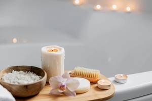 Eine Badewanne mit Kerzen, Seife, einer Orchidee und einem Handschuh in einem ruhigen Badezimmer.