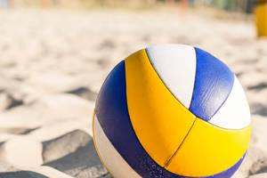 Ein Volleyball liegt auf einem Sandstrand, mit gelben, blauen und weißen Farben.