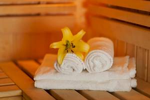 Eine Sauna mit Holzbank, drei weißen Handtüchern und einer gelben Blume.