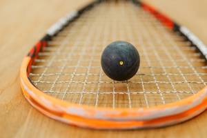 Ein orangefarbener Tennisschläger mit einem schwarzen Ball auf einem Holzboden.