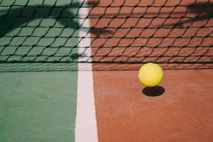Ein gelber Tennisball liegt auf einem Tennisplatz neben dem Netz.