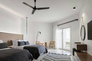 Doppelbettzimmer im Serry Beach Resort mit weißen Wänden, einer großen Glastür und einem Ventilator an der Decke.
