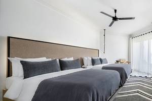 Zwei moderne Schlafzimmer im Serry Beach Resort mit weißen Wänden, Deckenventilator, Fernseher und Bettwäsche.