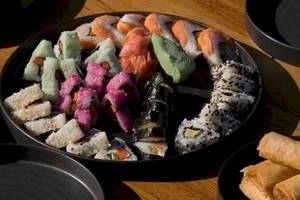 Ein großer Teller mit verschiedenen Sushi-Rollen und Springrollen auf einem Holztisch.