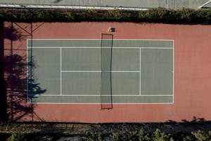 Ein Tennisplatz aus der Vogelperspektive mit roten Seitenwänden und einem Netz in der Mitte.