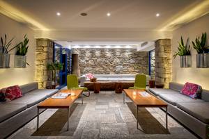 Innenbereich des Mykonos Theoxenia Boutique Hotels mit Steinwand, Sofas, Tischen und Pflanzen.