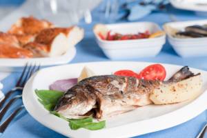 Ein gebratener Fisch auf einem weißen Teller mit Kartoffeln und Gemüse