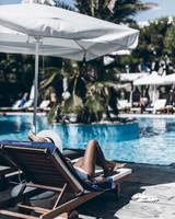 Gäste entspannen am Pool im Mykonos Theoxenia Boutique Hotel unter einem Sonnenschirm.
