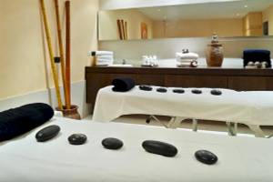 Spa-Behandlungsraum im Hipotels Mediterraneo mit zwei Massagetischen, schwarzen Steinen und einem großen Spiegel.