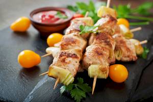 Gegrillte Hähnchen-Shashlik mit Gemüse und Sauce auf einem schwarzen Teller