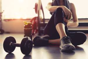 Eine Frau im Fitnessstudio ruht sich aus, neben ihr liegt eine Hantel und eine Wasserflasche.