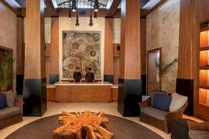 Hotellobby mit Holzelementen, modernen Möbeln, einem großen Holztisch und zwei Mitarbeitern hinter einer Rezeption.