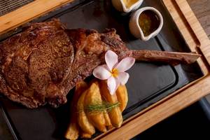 Ein gegrilltes Steak mit Rosmarin und Blumen auf einem schwarzen Teller.