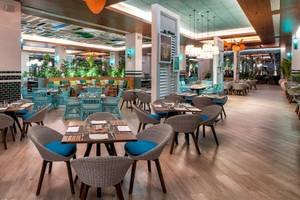 Innenansicht des Restaurants im Lopesan Costa Bavaro Resort Spa & Casino mit blauen Stühlen und Holztischen.