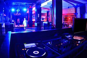 DJ-Pult in einem Nachtclub mit blauer Beleuchtung und Personen auf der Bühne.