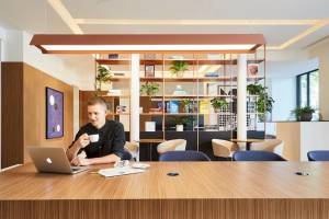 Ein Mann sitzt mit Laptop und Kaffee in einem Hotellobby.