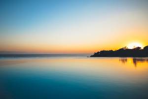 Sonnenuntergang über dem Meer mit einem kleinen Felsen in der Mitte, Club Marvy im Hintergrund