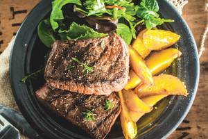 Ein Teller mit gegrilltem Steak und Pfirsichscheiben im Club Marvy Hotel.