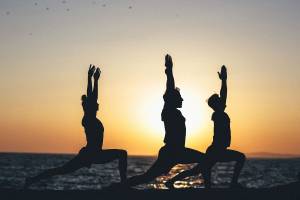 Drei Menschen in Yoga-Posen am Strand bei Sonnenuntergang.