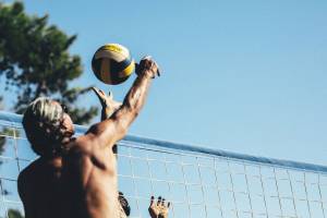 Zwei Männer spielen Volleyball vor einem Netz an einem sonnigen Tag.