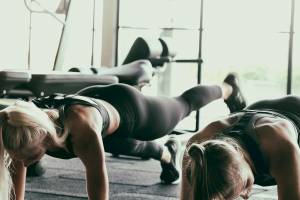 Zwei Frauen machen Push-Ups im Fitnessstudio mit Trainingsgeräten im Hintergrund.