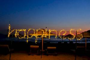 Lichterketten auf einem Strand, die 'Happiness' bilden, mit Club Marvy im Hintergrund.