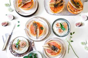 Mehrere Teller mit Fisch in Orangensaft und frischen Feigen auf einem Tisch angerichtet.