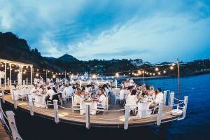 Dinnerparty auf einem Boot mit Gästen, die an langen Tischen sitzen, bei Nacht.