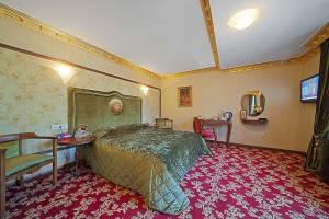 Ein elegantes Hotelzimmer mit einem großen Bett, grünen Kopfteilen, einem Tisch und Stühlen.