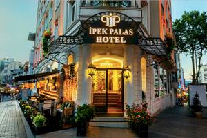 Außenansicht des Ipek Palas Hotels mit beleuchtetem Eingang und davor stehenden Tischen und Stühlen.