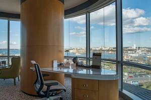 Innenansicht eines Zimmers im Doubletree by Hilton Istanbul Moda mit Schreibtisch, Stühlen und Panoramafenstern.