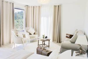 Wohnzimmer von L'Hostellerie du Moulin mit weißen Möbeln, heller Beleuchtung und Blick auf Bäume.