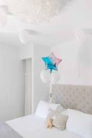 Ein Bett mit weißen Kissen und Ballons, darunter ein Teddybär auf einem gemusterten Kissen.