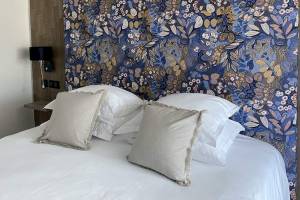 Ein Bett mit weißen Laken und Kissen vor einer blauen Blumentapete im Hotel La Lagune.