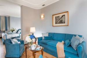 Innenansicht der Suite im Bettoja Hotel Mediterraneo mit blauem Sofa, Tisch, Blumenvase und Bild an der Wand.