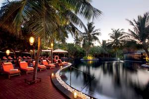 Pool-Lounge-Bereich im Sun Siyam Iru Fushi Hotel mit roten Liegestühlen und Palmen.