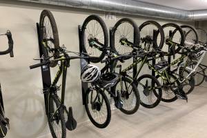 Fahrräder sind in einer Reihe in einer Garage aufgehängt, darunter ein Fahrrad mit Helm, das an einem schwarzen Ständer befestigt ist.