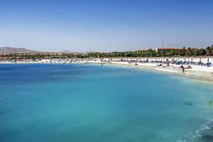 Strand mit vielen Menschen und blauem Wasser vor dem Barcelo Fuerteventura Castillo Hotel.