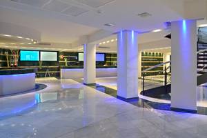 Hotellobby von Sol Milanos Pinguinos mit Empfangstresen, Monitoren und einer Wendeltreppe.