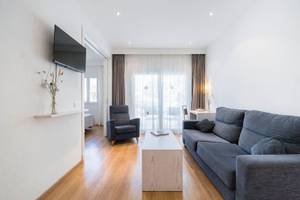 Wohnzimmer des Princesa Playa Hotels mit einem Fernseher an der Wand, einem Sofa, einem Stuhl und einem Tisch.