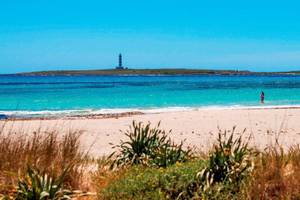 Strand mit Leuchtturm im Hintergrund und einer Person im Wasser, Punta Prima Resort & Spa.