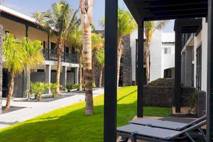 Außenbereich des Barcelo Fuerteventura Castillo Hotels mit gepflegtem Rasen, Steinwänden und Palmen.
