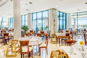 Innenansicht des Restaurants im Punta Prima Resort & Spa mit gedeckten Tischen und großen Fenstern.