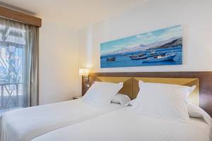 Doppelzimmer mit Meerblick im Barcelo Fuerteventura Castillo Hotel mit zwei weißen Betten, einer Wand mit einem Gemälde von Booten und Bergen.