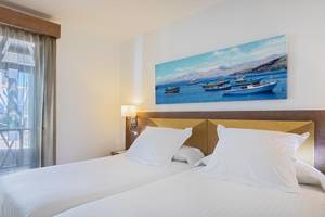 Doppelzimmer mit Meerblick im Barcelo Fuerteventura Castillo Hotel mit zwei Betten, weißem Dekor und einem Gemälde von Booten auf See.