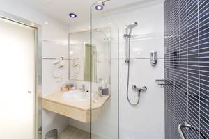 Badezimmer des Globales Lord Nelson Hotels mit Glasdusche, Waschbecken und Spiegel.