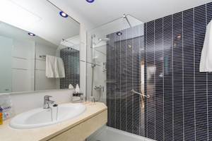 Ein Badezimmer im Hotel Globales Lord Nelson mit einer Dusche, einem Waschbecken und Spiegel.